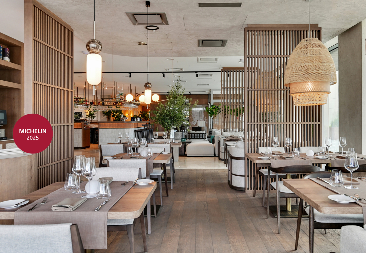 Hotel restaurant awarded Michelin 2025, with wooden screens, set tables, woven pendant lights and a central bar in a warm modern interior
