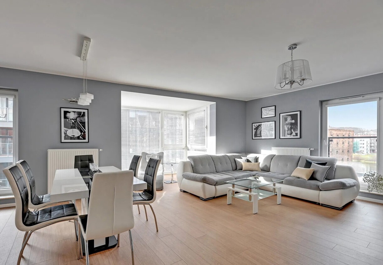 Modern living-dining suite with gray sectional sofa, glass coffee table, dining table with leather chairs and large city-view windows