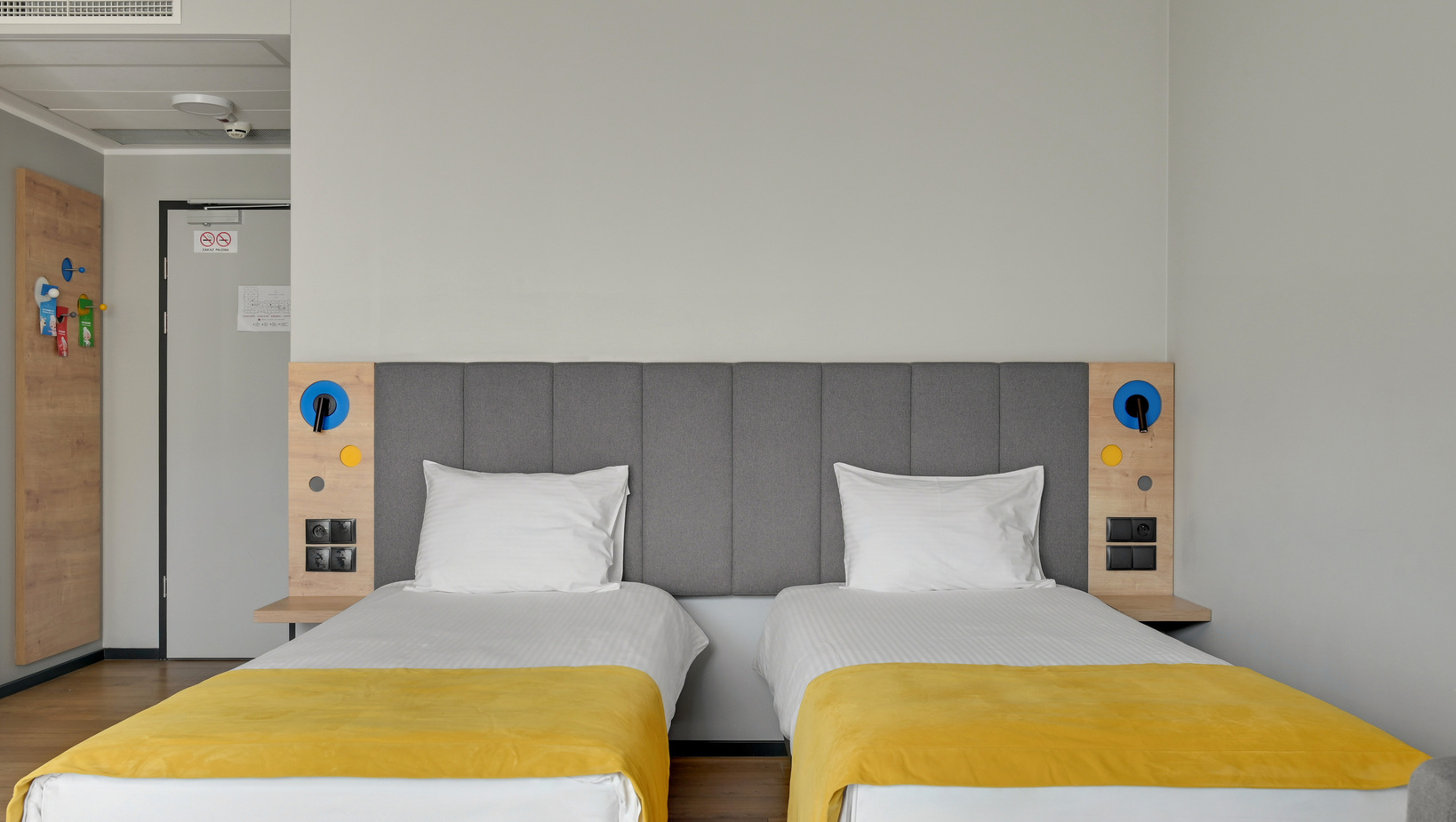 Twin beds with grey padded headboard, yellow runners, bedside panels with reading lights and power outlets