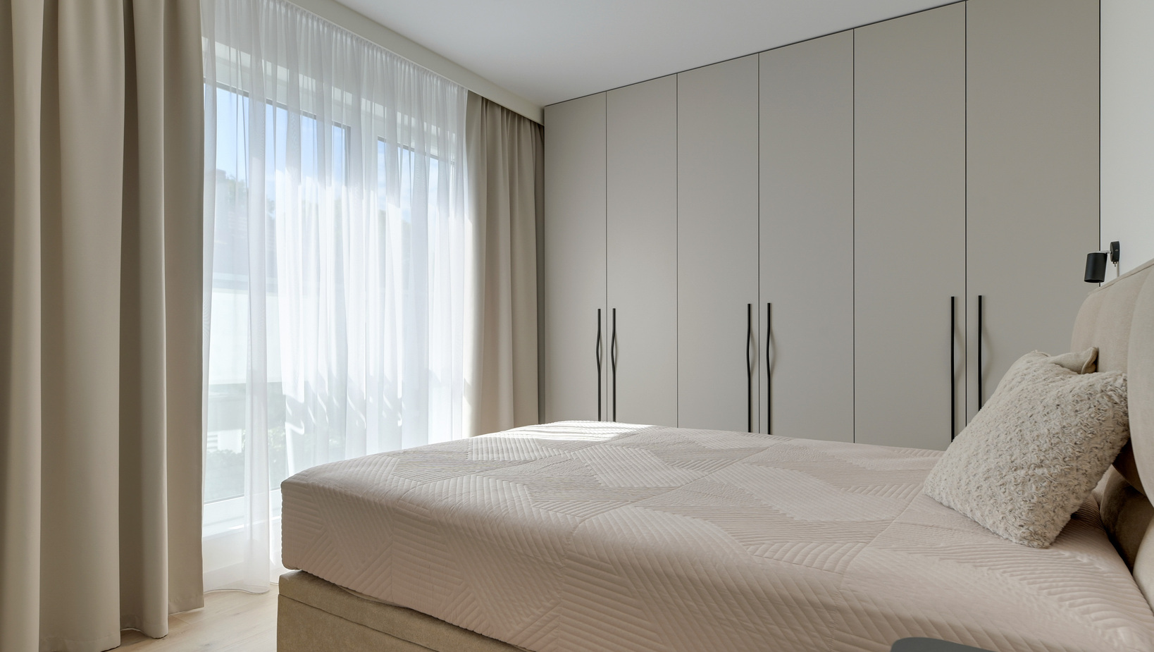 Jasna, nowoczesna sypialnia hotelowa z dużą szafą, jasnymi i ciemnymi zasłonami, pikowanym łóżkiem i poduszkami.