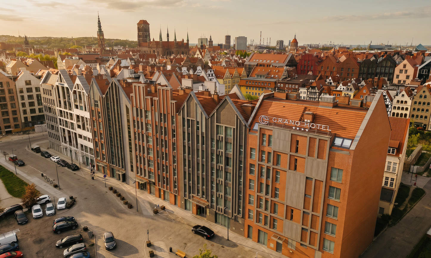 Grano Hotel's red-brick façade with pitched gables facing a historic Old Town skyline of church spires and harbor.