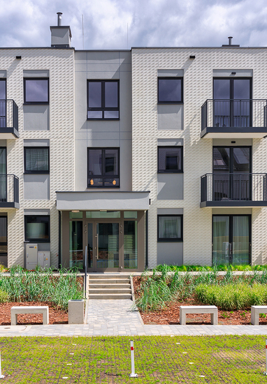 Modern three-story hotel facade with balconies, landscaped entrance, benches and paved walkway