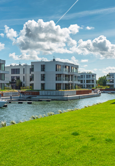 Nowoczesne apartamenty nad wodą z przeszklonymi balkonami, prywatną mariną i zacumowaną łodzią przy zadbanym trawniku.