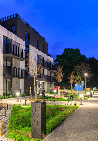 Modern hotel courtyard at dusk with lit pathways, balcony rooms, grassy landscaping and benches for guests.