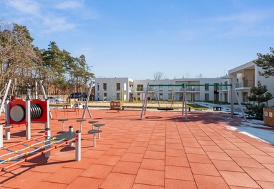 Outdoor family playground with swings and climbing equipment on red safety tiles, set before modern white hotel rooms