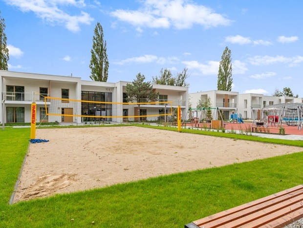 Modern low-rise hotel suites with balconies overlooking a sand volleyball court, children's playground and landscaped lawns.
