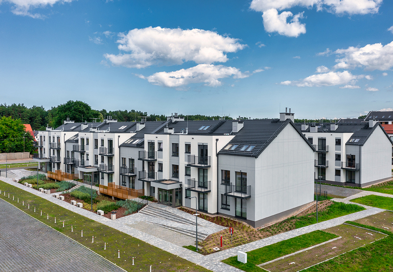 Modern three-story buildings with private balconies, paved walkways, landscaped courtyard and forested backdrop