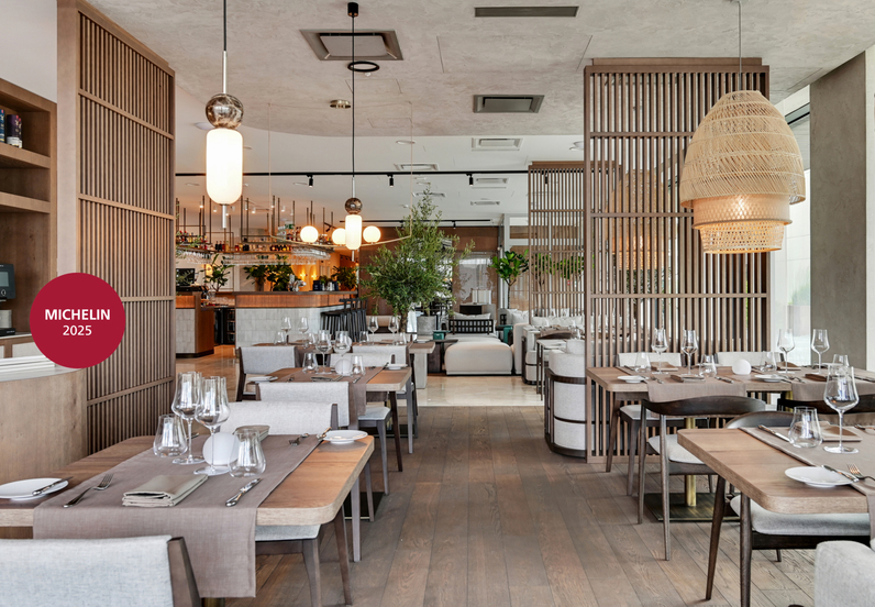 Hotel restaurant awarded Michelin 2025, with wooden screens, set tables, woven pendant lights and a central bar in a warm modern interior