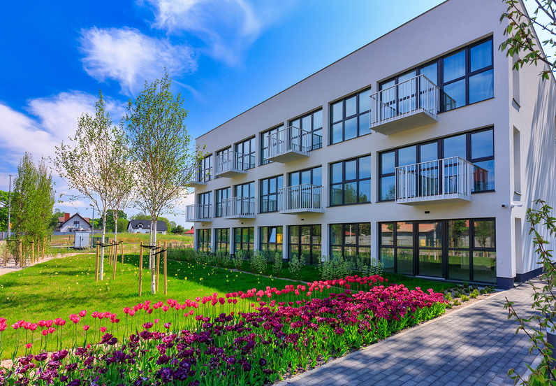 Modern three-story hotel with glass-front rooms and small balconies, manicured lawn, colorful tulip beds and paved walkway.