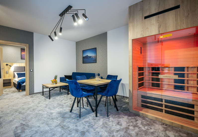 Apartament z jadalnią i niebieskimi aksamitnymi krzesłami, osobną sypialnią i przeszkloną sauną w czerwonym świetle.