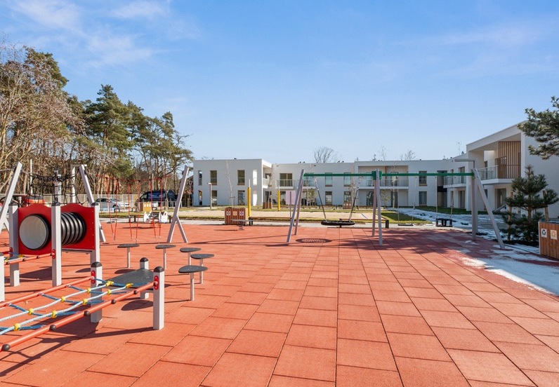 Outdoor family playground with swings and climbing equipment on red safety tiles, set before modern white hotel rooms