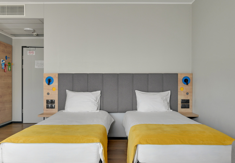 Twin beds with grey padded headboard, yellow runners, bedside panels with reading lights and power outlets