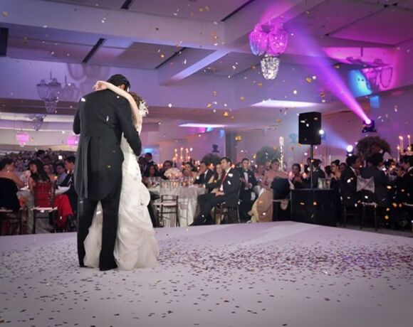 Recepción de boda elegante con novia y novio bailando en pista cubierta de confeti en salón amplio con invitados sentados y luces ambientales