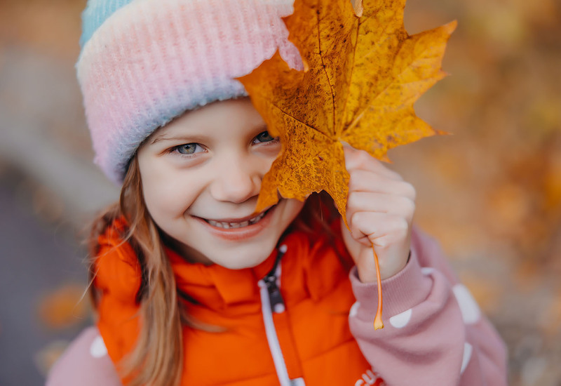 A smiling girl in a hat covering one eye with an autumn leaf during her stay at Green Mountain Hotel***** & Apartments in Karpacz.
