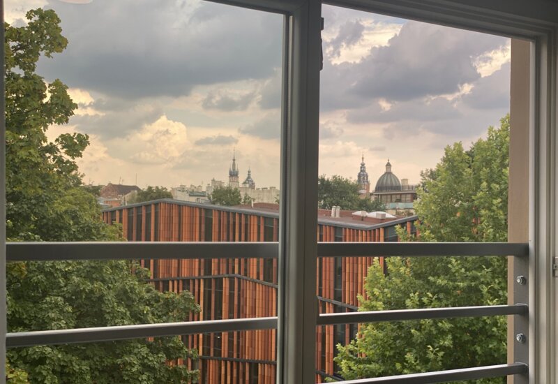 Widok z okna na piętrze. Z przodu budynek biblioteki. W tle dachy krakowskich budynków.