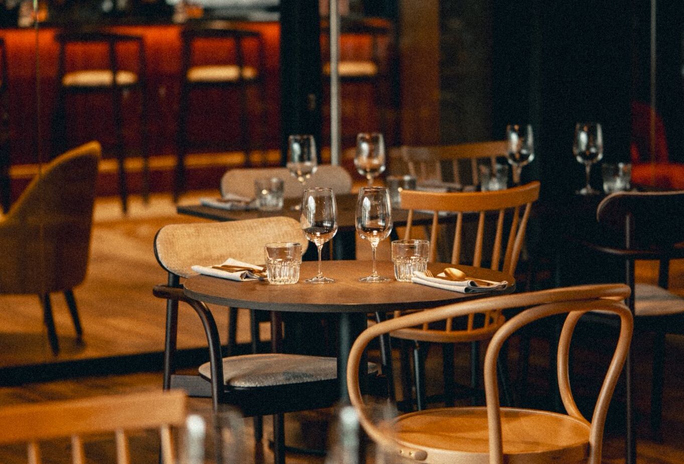 Przytulna restauracja hotelowa z drewnianymi stołami i krzesłami, bursztynowymi lampami, nakryciami i oświetlonym barem w tle