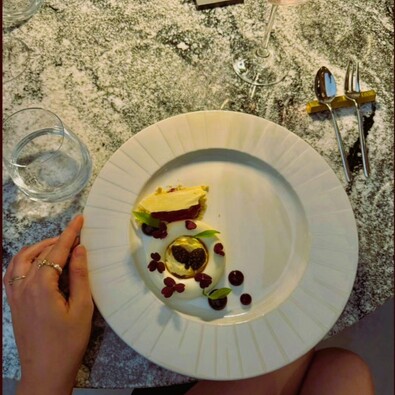 Deser degustacyjny: mus z kropkami czekolady, jadalne kwiaty i microgreens na białym talerzu, kieliszek na marmurowym stole