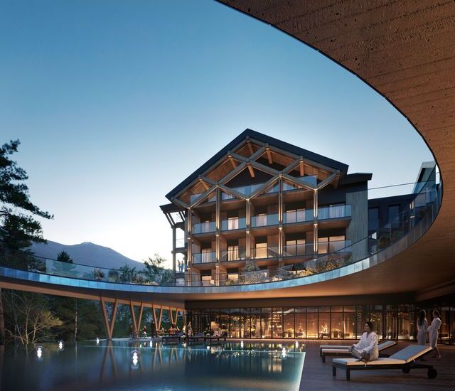 Nowoczesny górski hotel z drewnianą konstrukcją i balkonami, podświetlonym basenem, tarasem z leżakami i gośćmi w szlafrokach.