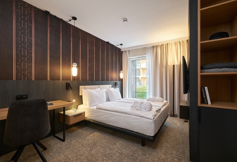 Moderní dvoulůžkový pokoj s bílým ložním prádlem, složenými župany, závěsnými lampami, pracovním stolem a výhledem z balkonu