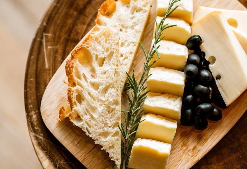 Krojony rzemieślniczy chleb, plastry miękkiego sera, czarne oliwki i gałązka rozmarynu na drewnianej desce — hotelowa przystawka.