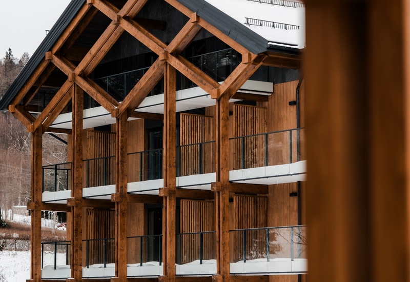Hotel w stylu chalet z drewnianą konstrukcją, balkonami ze szklanymi balustradami i śniegiem
