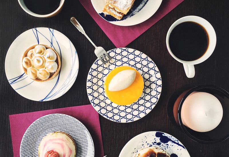 Różne wypieki — tarty, musowe kopułki i plaster ciasta z cynamonem — z dwiema czarnymi kawami na ciemnym drewnianym stole