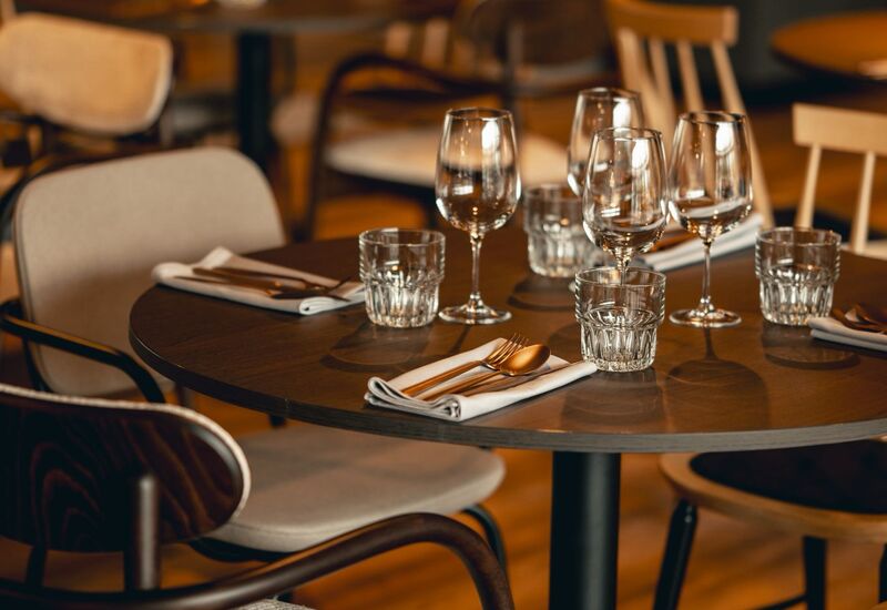 Przytulny stół w restauracji z kieliszkami do wina, szklankami, złożonymi serwetkami i drewnianymi krzesłami w ciepłym świetle
