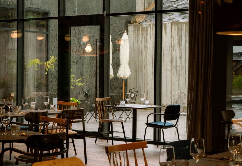 Przytulna restauracja hotelowa z nakrytymi stołami i kieliszkami, przeszklone ściany prowadzą na taras ze złożonymi parasolami