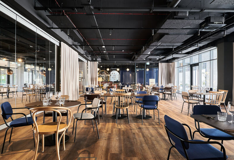 Nowoczesna restauracja hotelowa z drewnianą podłogą, mieszanymi krzesłami, dużymi oknami, nakrytymi stołami i barem z tyłu