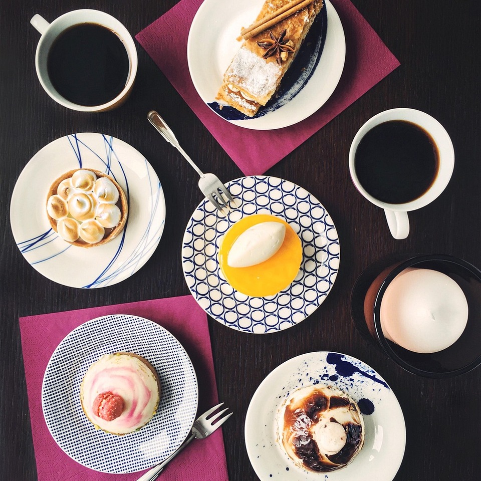 Różne wypieki — tarty, musowe kopułki i plaster ciasta z cynamonem — z dwiema czarnymi kawami na ciemnym drewnianym stole