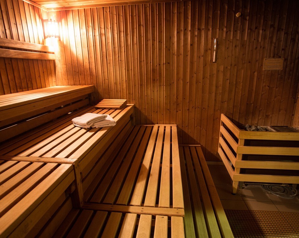 Sauna w hotelu z drewnianymi panelami, piętrowymi ławkami, ciepłym oświetleniem, ręcznikami i piecem z kamieni