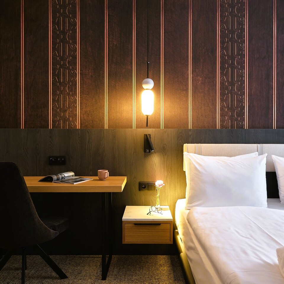 Nowoczesny pokój hotelowy z dwiema łóżkami, białą pościelą, zagłówkiem, drewnianą ozdobną ścianą, lampą, stolikiem nocnym i biurkiem.
