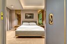 Modern hotel bedroom with king bed, upholstered headboard, bedside tables and lamps, fresh flowers, soft recessed ceiling lighting and neutral decor