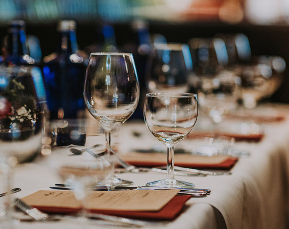 Elegant dining table with white linen, wine and water glasses, folded menus, candlelight and blue bottles creating a warm, intimate atmosphere