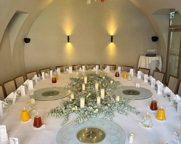 Runder Banketttisch für Hochzeit mit Eukalyptus- und Kerzenarrangement, gläsernen Drehplatten, Saftkaraffen, gewölbte Decke und warmes Licht