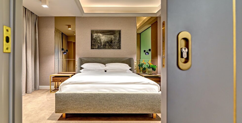 Modern hotel bedroom with king bed, upholstered headboard, bedside tables and lamps, fresh flowers, soft recessed ceiling lighting and neutral decor