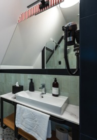 Nowoczesna łazienka hotelowa ze zlewem, dużym lustrem i eleganckimi zielonymi płytkami ściennymi.