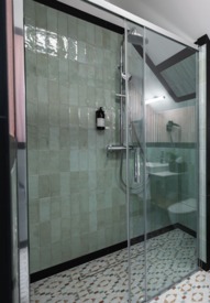 Nowoczesna łazienka hotelowa z prysznicem, toaletą, dużym lustrem i zieloną rośliną na białej umywalce