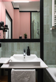 Nowoczesna łazienka hotelowa z zielonymi kafelkami, lustrem, umywalką, suszarką do włosów i wanną z białym ręcznikiem