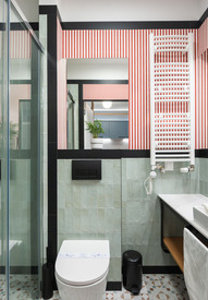 Hotelowa łazienka z deszczownicą w szklanej kabinie, miętowymi kafelkami, czerwonym paskiem, podgrzewaczem ręczników, umywalką i WC