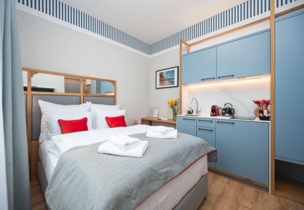 Przytulny pokój hotelowy z wygodnym łóżkiem, niebieską kuchnią, drewnianym biurkiem i jasnym, nowoczesnym wystrojem.