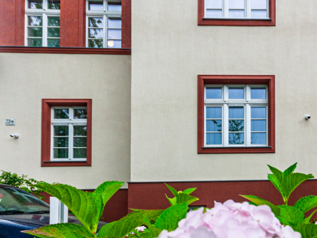Fragment elewacji hotelu z czerwonymi ramami okien i kwitnącymi na różowo hortensjami na pierwszym planie
