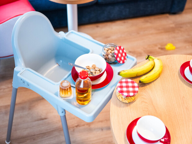 Krzesło do karmienia z miseczką, butelką miodu i przekąskami przy drewnianym stole z bananami i filiżankami