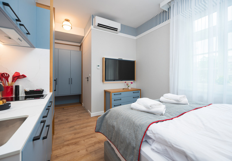 Kompaktowy pokój hotelowy ze strefą kuchenną, łóżkiem z ręcznikami, telewizorem, klimatyzacją i jasnym oknem