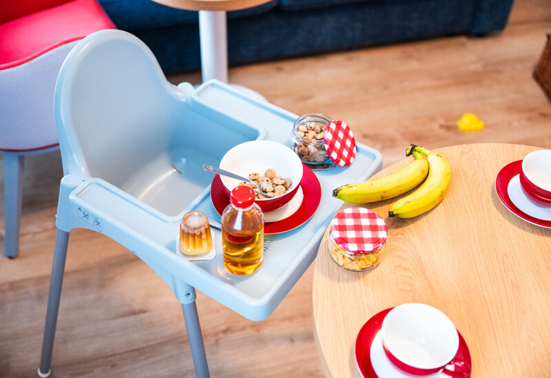 Krzesło do karmienia z miseczką, butelką miodu i przekąskami przy drewnianym stole z bananami i filiżankami