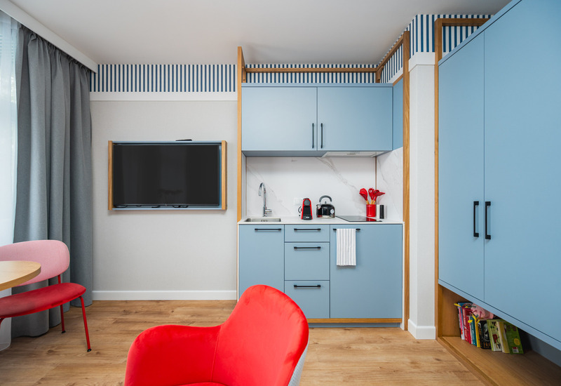 Aneks kuchenny z błękitnymi szafkami, marmurowym panelem, ekspresem do kawy, telewizorem, czerwonymi fotelami i drewnianą podłogą.