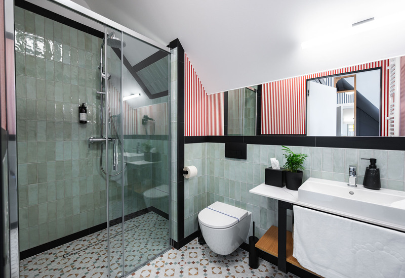 Nowoczesna łazienka hotelowa z przeszklonym prysznicem walk-in, deszczownicą, wiszącą toaletą, umywalką i wzorzystą podłogą