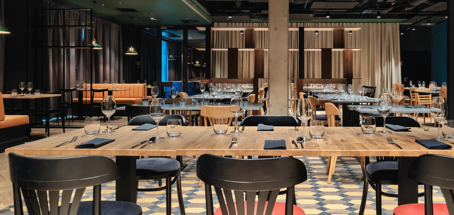 Nowoczesna restauracja z drewnianymi stołami, mieszanymi czarnymi i czerwonymi krzesłami, elegancko zastawionymi na kolację