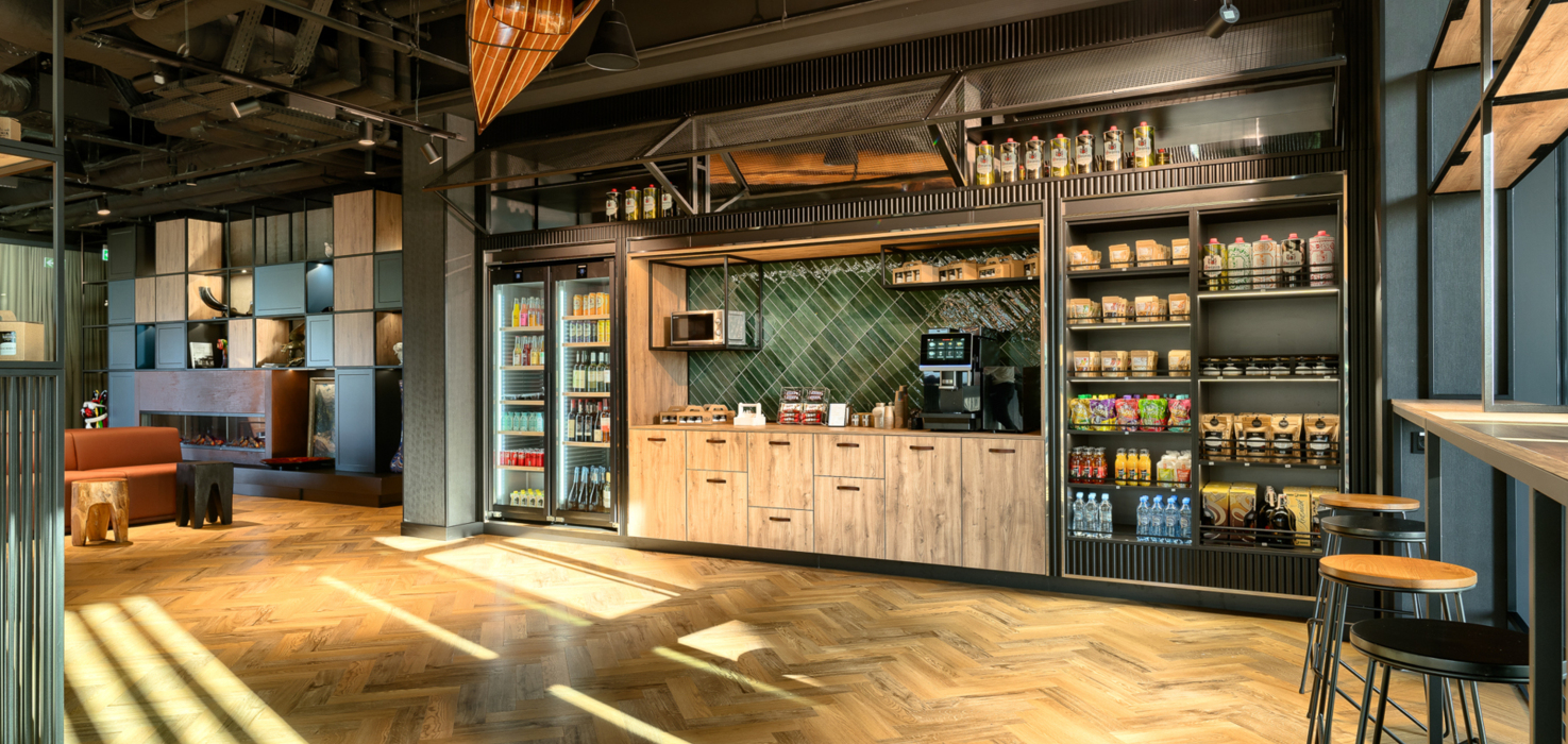 Nowoczesny hotelowy sklepik z drewnianymi meblami, chłodziarkami z napojami i wygodnymi stołkami barowymi.