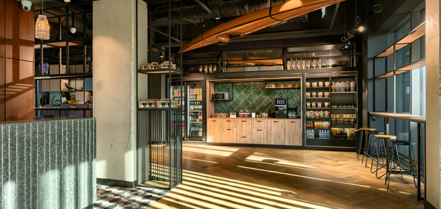 Nowoczesny hotelowy sklepik z drewnianymi meblami, ekspres do kawy, przekąski i miejsce do siedzenia przy dużych oknach